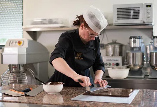 chocolatier en train de travailler le chocolat sur un plan de travail en cuisine professionnelle