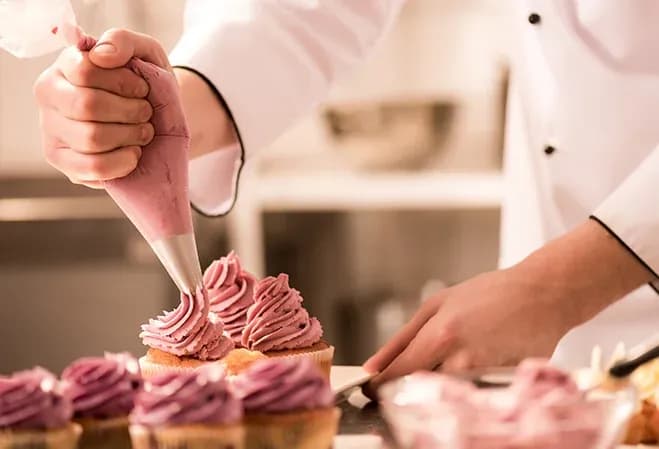 pâtissier décorant des cupcakes avec de la crème violette à l'aide d'une poche à douille