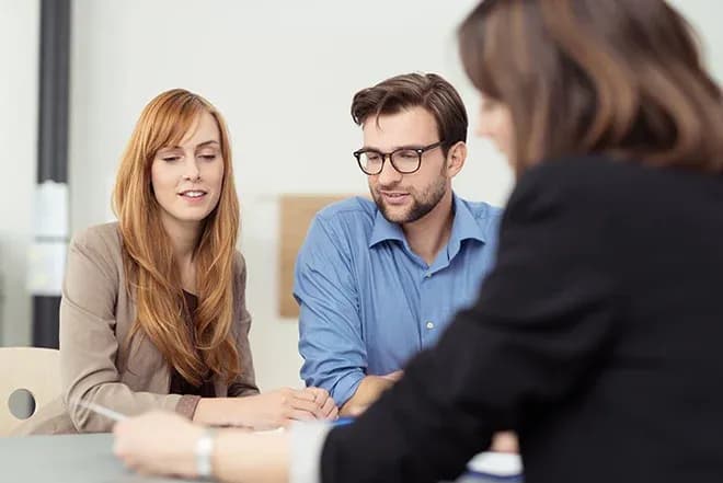 discussion entre trois personnes autour d'une table avec des documents et un ordinateur portable