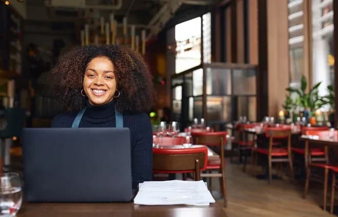 femme souriante assise devant un ordinateur portable dans un restaurant élégant