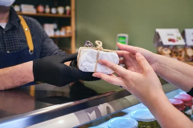 un client reçoit un fromage emballé dans un magasin avec des produits en arrière-plan