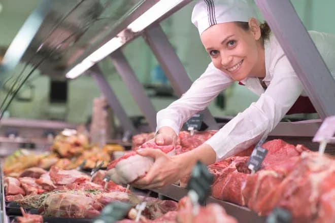 vendeuse en boucherie souriante présentant une pièce de viande au comptoir