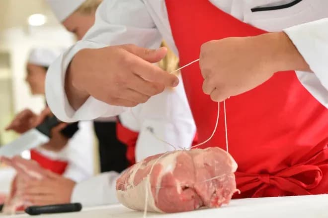 apprenti charcutier en train de ficeler un morceau de viande sur une table de travail
