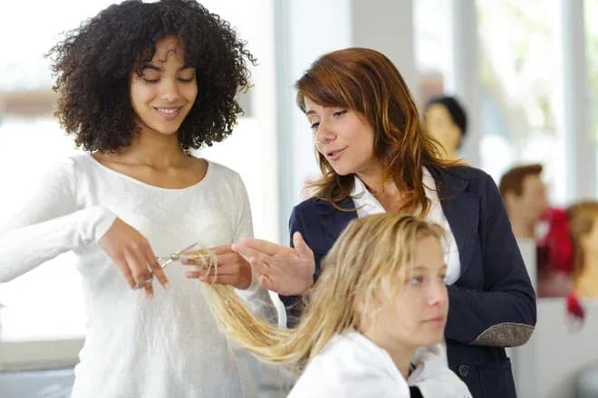 apprentie coiffeuse coupant des cheveux sous l'œil attentif d'une formatrice dans un salon de coiffure