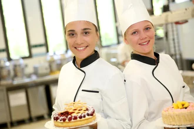deux apprenties pâtissières souriantes tenant des gâteaux dans une cuisine