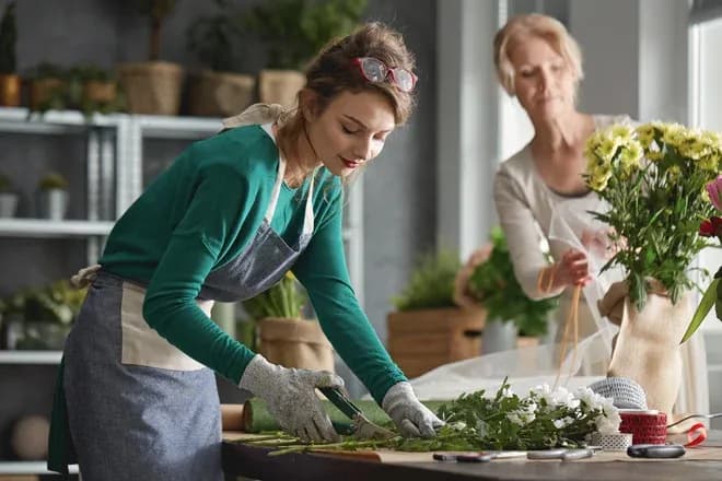 apprentie fleuriste coupant tiges pendant qu'une collègue prépare des bouquets