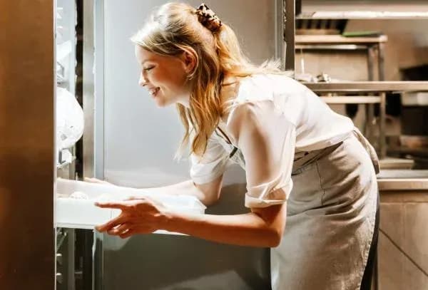 employée de cuisine sort un plateau d'un réfrigérateur professionnel