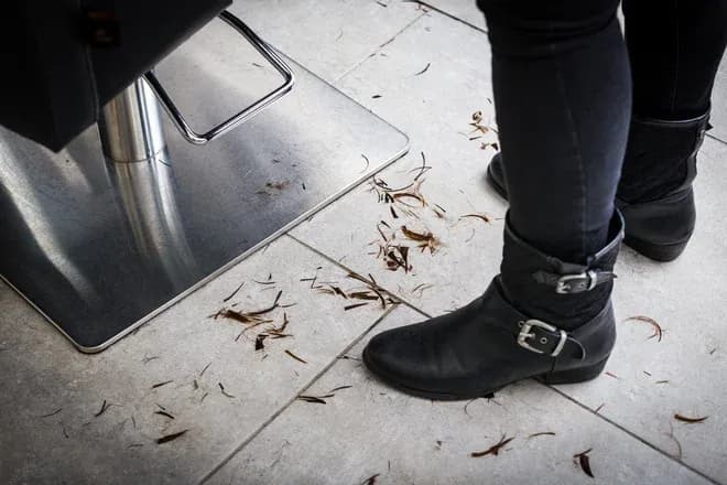 pied d'une personne en bottines noires près d'un sol avec des cheveux coupés