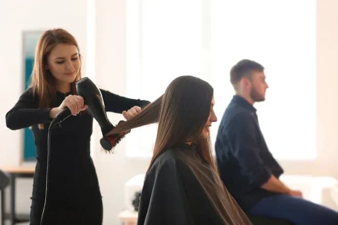 Coiffeuse utilisant un sèche-cheveux sur les cheveux d'une cliente en salon de coiffure