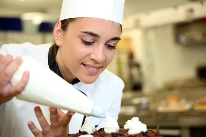jeune pâtissière décore un gâteau avec de la crème chantilly en cuisine