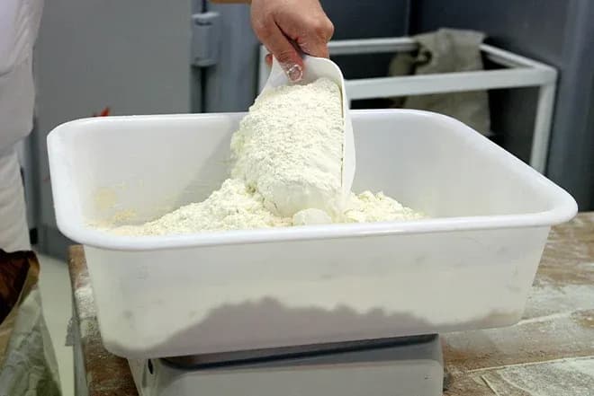 main versant de la farine dans une cuve sur balance de boulangerie