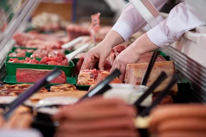 main d'un charcutier sélectionnant des morceaux de viande dans un étal de boucherie
