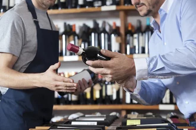caviste présentant une bouteille de vin à un client devant des rayonnages