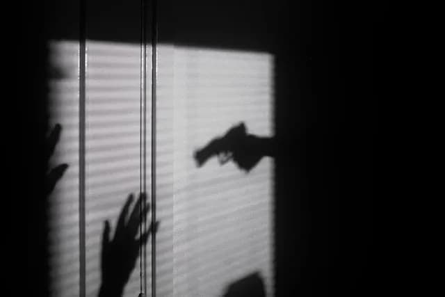 ombres de mains et d'une arme projetées sur un mur avec des rayures de lumière