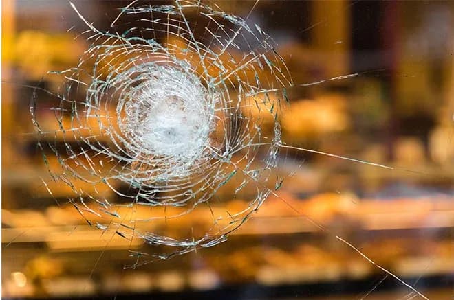 impact circulaire et fissures rayonnantes sur vitre floutée d'une boulangerie