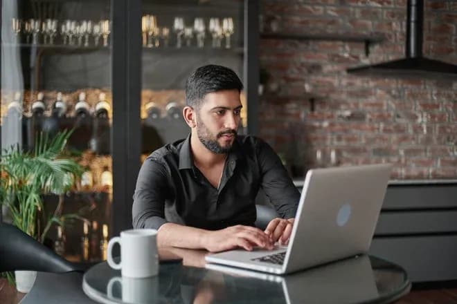 Homme concentré devant un ordinateur portable dans un intérieur moderne avec des bouteilles de vin en arrière-plan