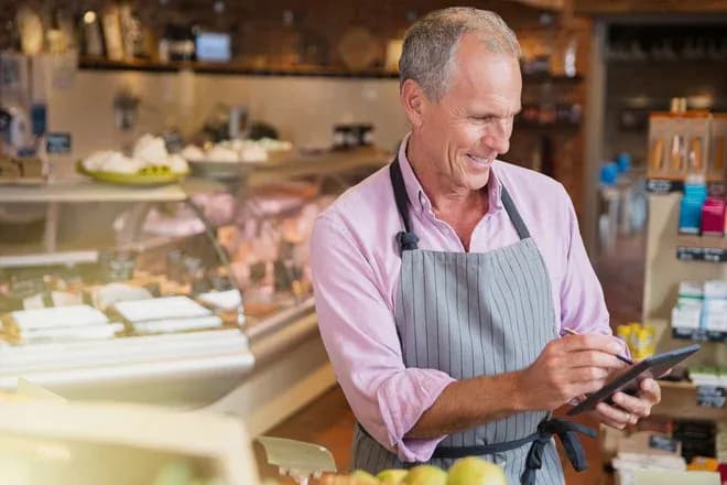 propriétaire d'épicerie en tablier utilisant une tablette au comptoir