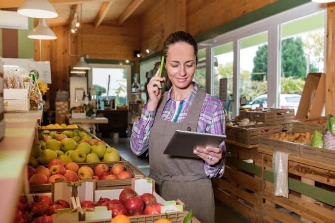 femme dans un magasin de fruits utilisant une tablette tout en parlant au téléphone