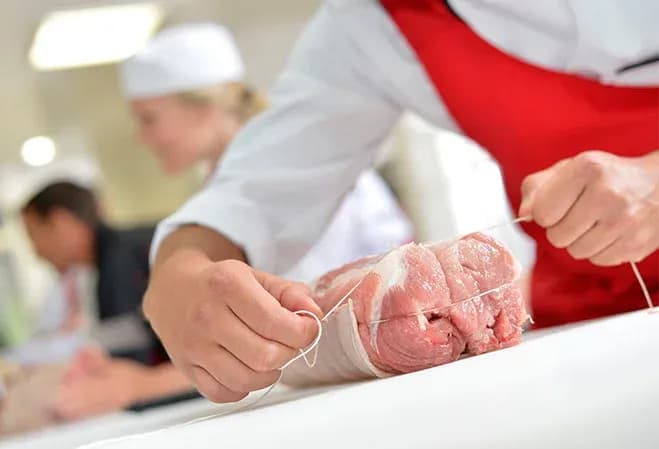 boucher ficelant un rôti cru avec de la ficelle sur un plan de travail