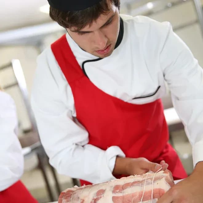 apprenti charcutier en tablier rouge noue un rôti de porc avec de la ficelle