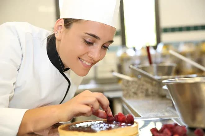 pâtissière souriante posant des framboises sur une tarte en cuisine