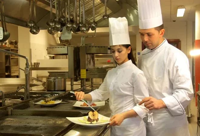 Chef en cuisine préparant un plat avec une assistante dans un restaurant moderne
