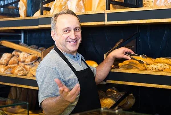 boulanger souriant en tablier prenant des pains avec une pince