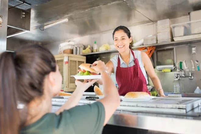 vendeuse souriante dans un food truck tendant un burger à une cliente