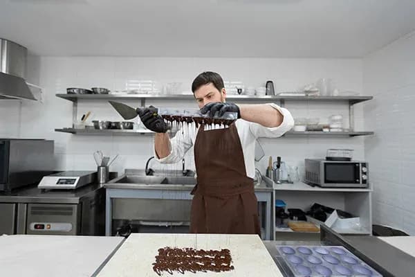 artisan chocolatier étalant du chocolat fondu sur un plan de travail en cuisine professionnelle