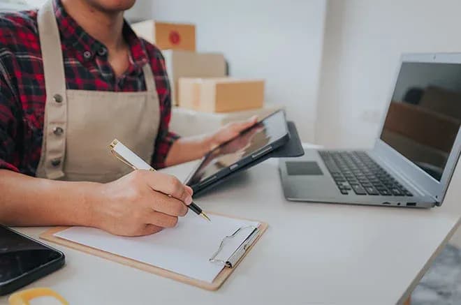 personne prenant des notes sur un carnet avec une tablette et un ordinateur portable sur un bureau