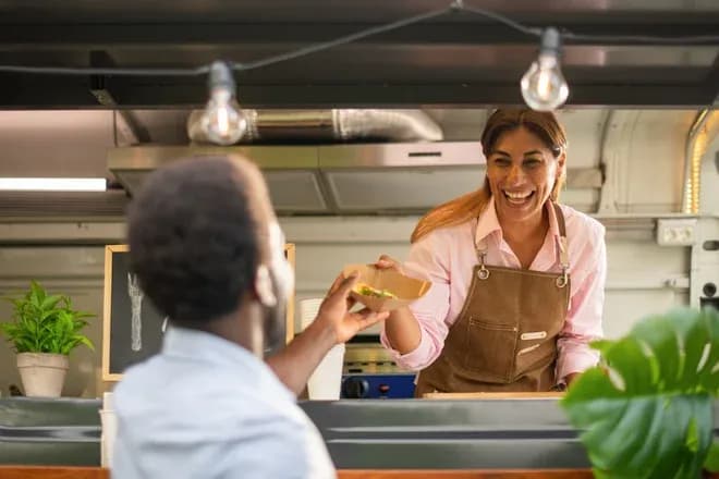 femme souriante servant un plat à un client dans un food truck convivial