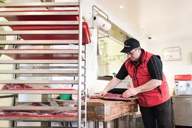boucher en gilet rouge tranche une pièce de viande sur une planche