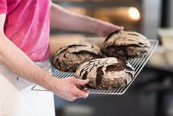 Boulanger tenant une grille avec plusieurs pains sortis du four dans une boulangerie.