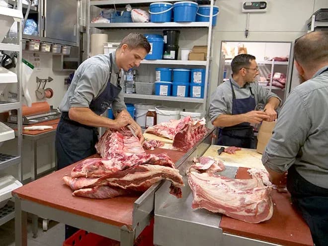 bouchers découpant des pièces de viande sur des plans de travail dans un atelier