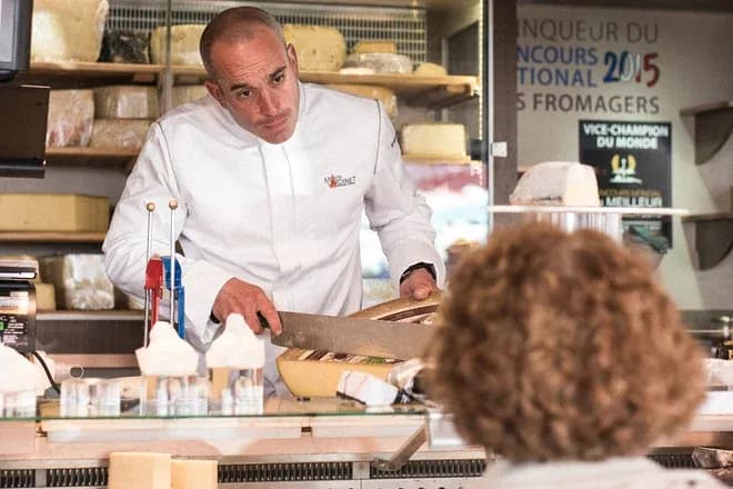 fromager tranche un morceau de fromage au comptoir devant un client