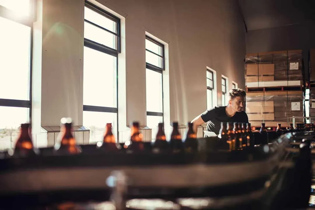 homme observant des bouteilles de bière dans un environnement lumineux et industriel