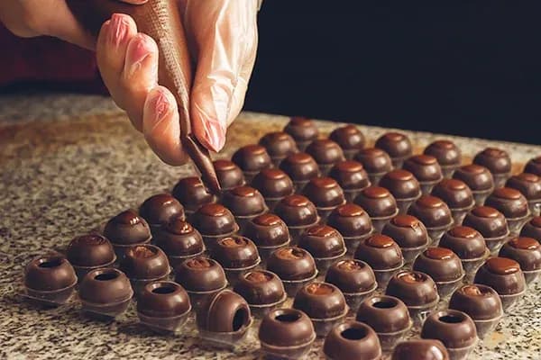 main d'une personne en train de remplir des chocolats sur une surface en marbre