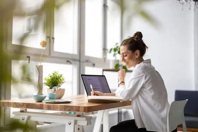 femme souriante travaillant sur un ordinateur portable à un bureau lumineux avec des plantes