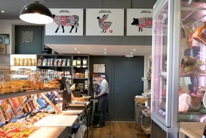 intérieur de boucherie affichant étals de viande et de pain avec un boucher au comptoir