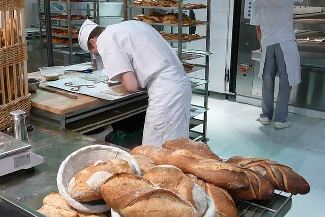 deux boulangers préparant pains et viennoiseries avec étagères remplies