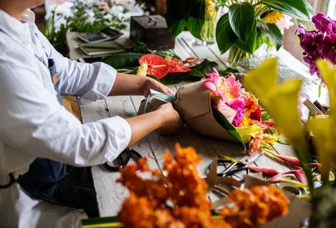 artisan floriste prépare un bouquet coloré sur une table de travail entourée de fleurs et d'outils