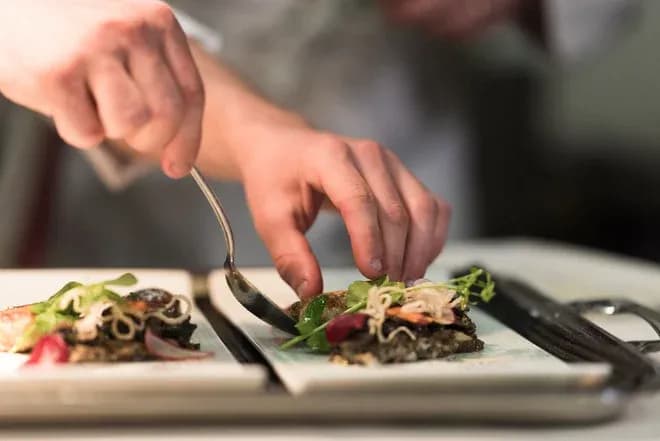 mains d'un chef dressant des amuse-bouches sur assiettes rectangulaires