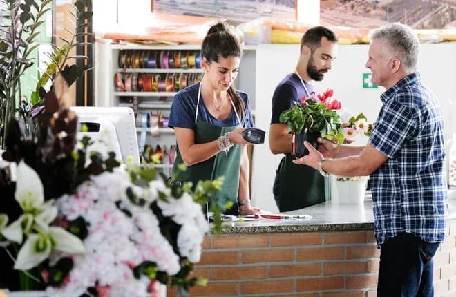 vendeuse scannant une plante en pot pour un client au comptoir d'une boutique de fleurs