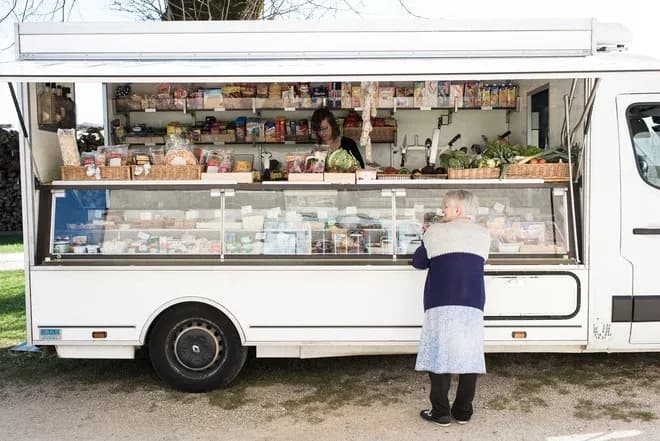 épicerie ambulante blanche avec vendeuse et cliente âgée devant étal de produits