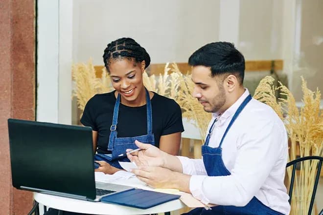 deux personnes souriantes discutent devant un ordinateur portable dans un café