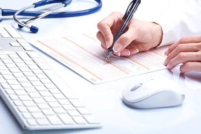 médecin remplissant une feuille d'arrêt maladie sur un bureau