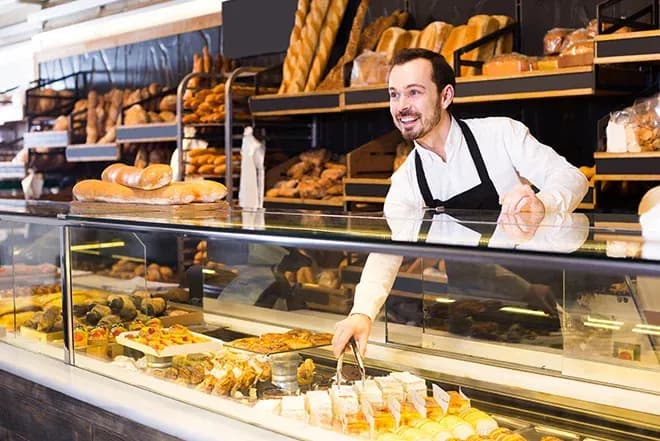 boulanger souriant sert des pâtisseries et pains dans une vitrine
