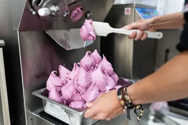 Préparation de glace rose dans un bac à l'aide d'une spatule en cuisine professionnelle