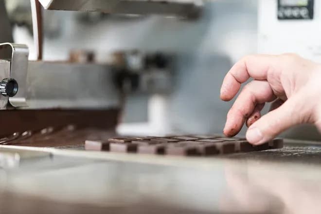 main d'un chocolatier manipulant des chocolats sur une machine de production