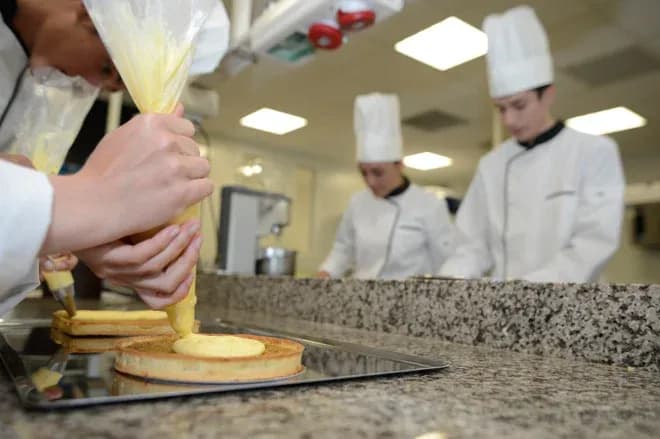 pâtissier en formation prépare un gâteau avec de la crème sur un plan de travail en cuisine